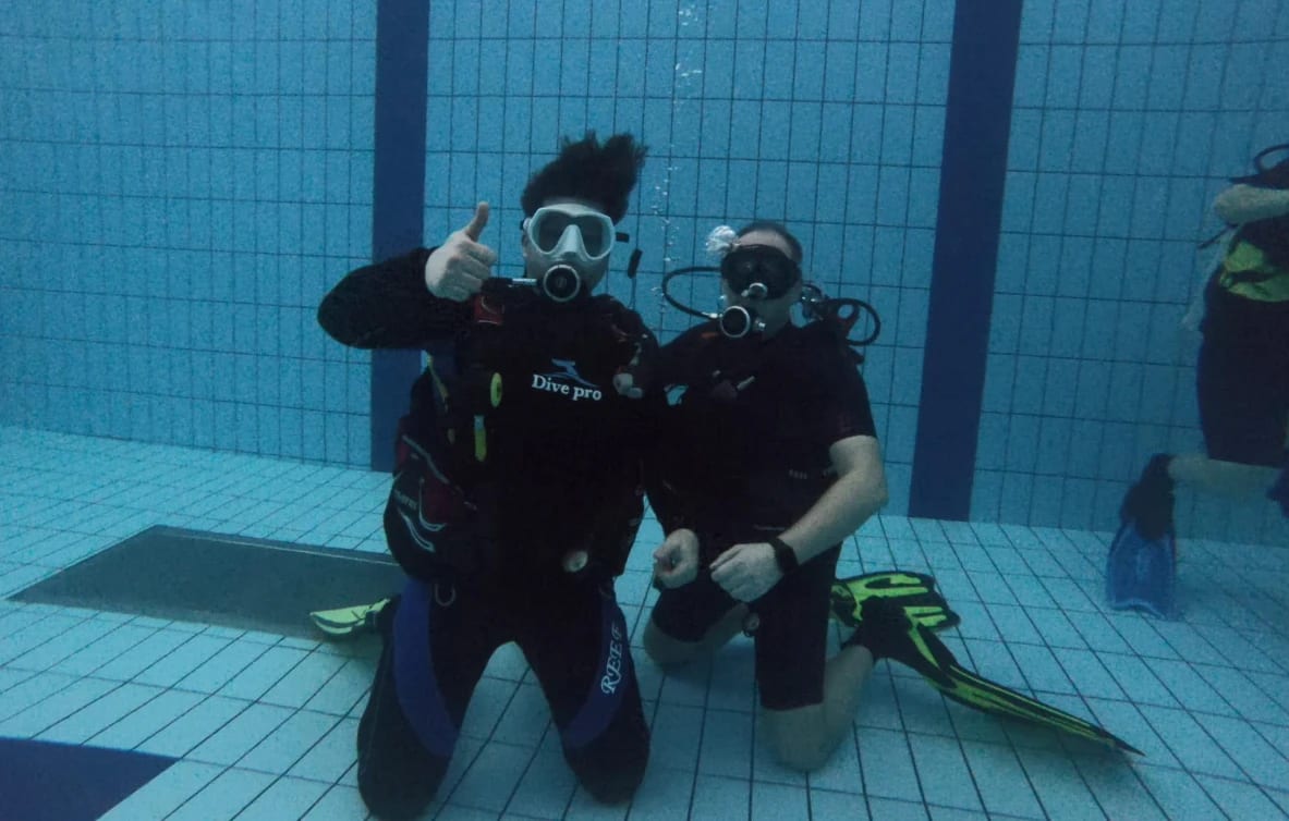 Doi scafandri îngenunchiați pe fundul piscinei, în timpul unui exercițiu